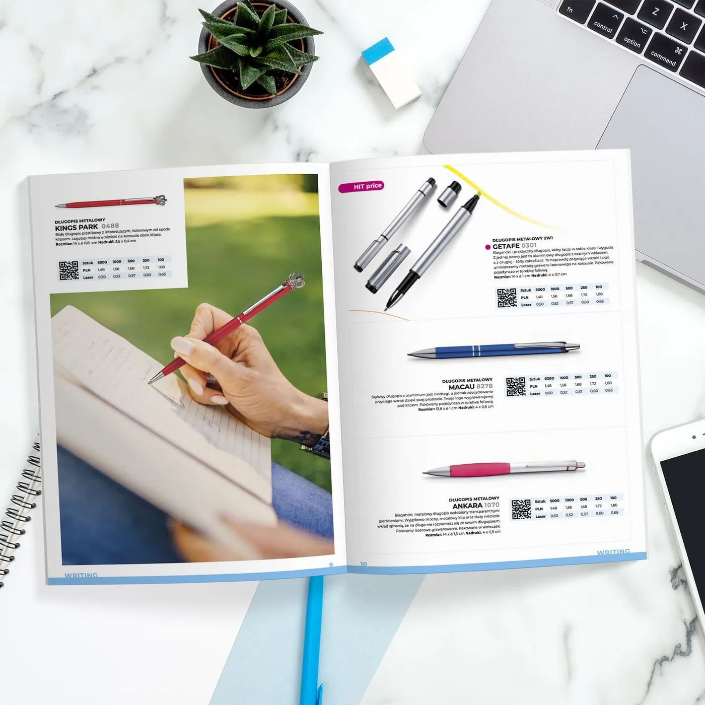 Macma - rozkładówka „Writing" na biurku obok laptopa i sukulenta: metalowe długopisy z cenami hurtowymi po lewej oraz zdjęcie dłoni piszącej długopisem w plenerze po prawej.