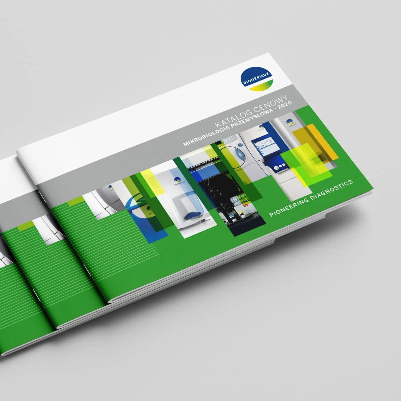 Stos egzemplarzy katalogu bioMérieux „Katalog Cenowy. Mikrobiologia Przemysłowa - 2020" z logo firmy i napisem „Pioneering Diagnostics" na zielonej okładce ze zdjęciami aparatury laboratoryjnej.