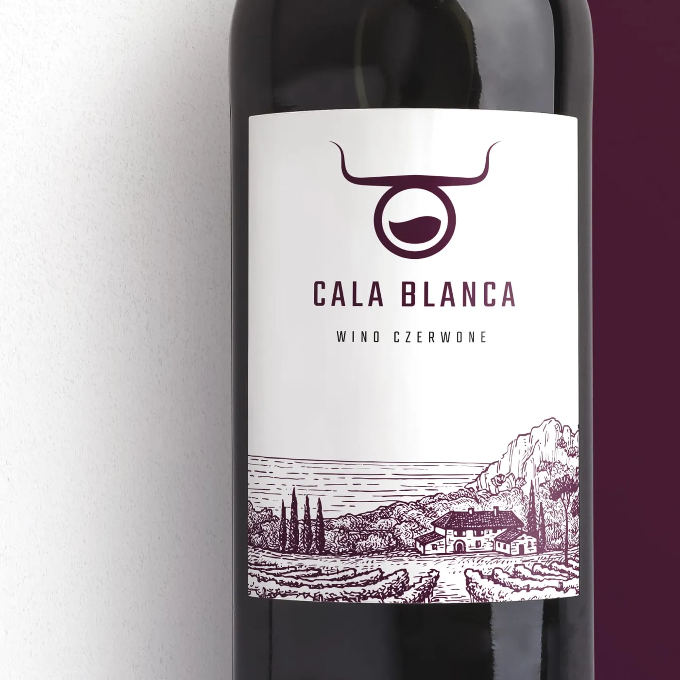 Zbliżenie etykiety wina Cala Blanca - logo byczej głowy, napis „CALA BLANCA. WINO CZERWONE" oraz rysunkowa ilustracja nadmorskiego krajobrazu z zatoką, klifem i domami.