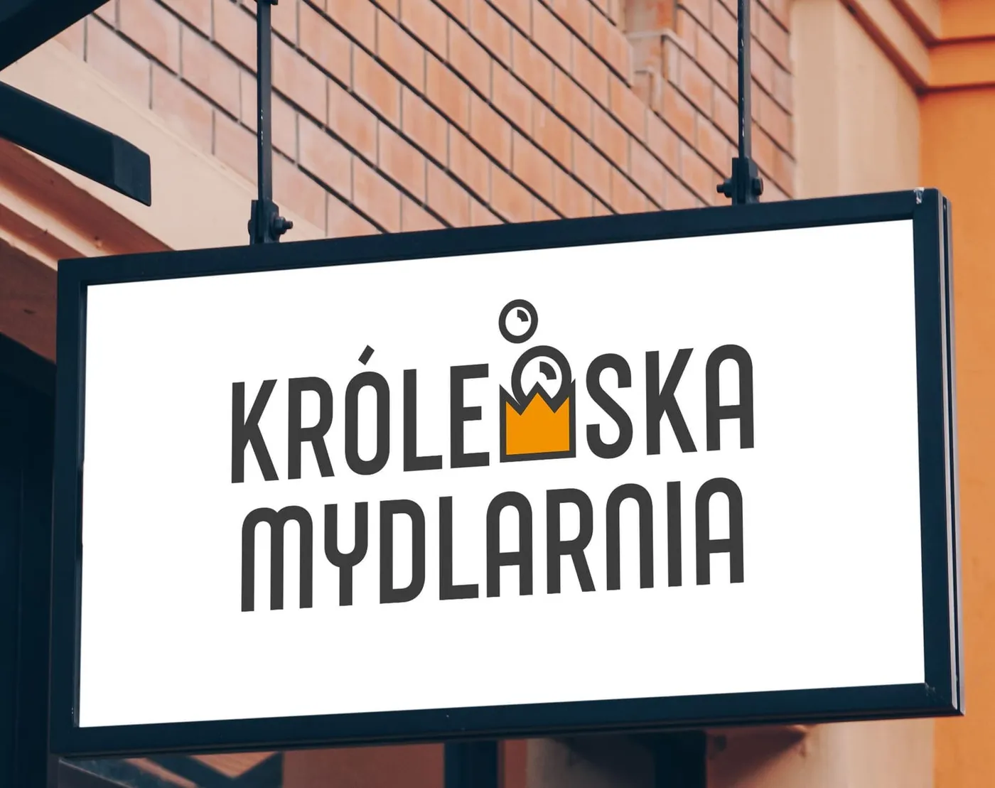 Królewska Mydlarnia - podświetlany szyld reklamowy z logotypem marki, zawieszony na wsporniku na fasadzie ceglanego budynku.