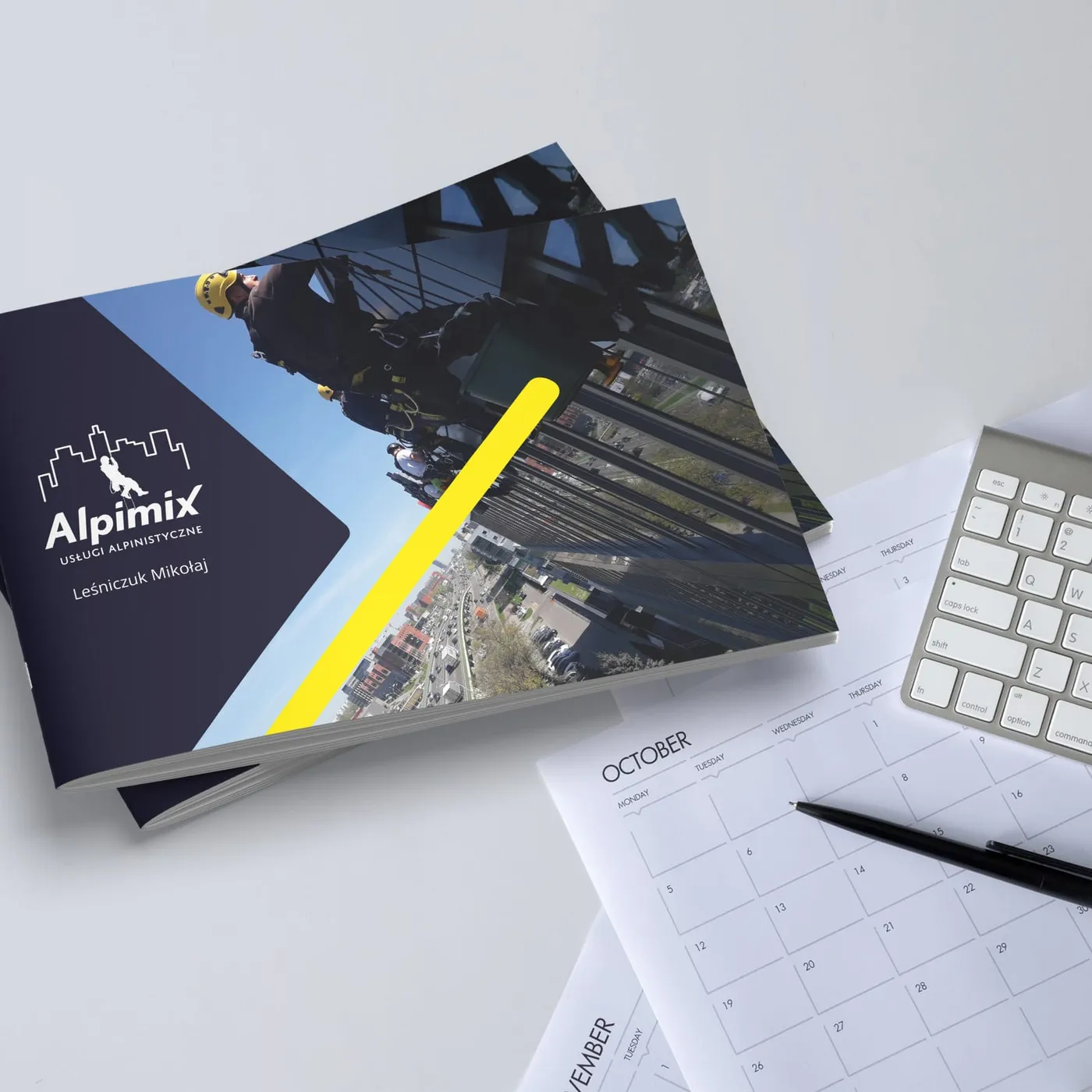 Alpimix - folder rozłożony na biurku obok okularów i kawy: strona z listą usług wysokościowych i zdjęciem pracy na linach.