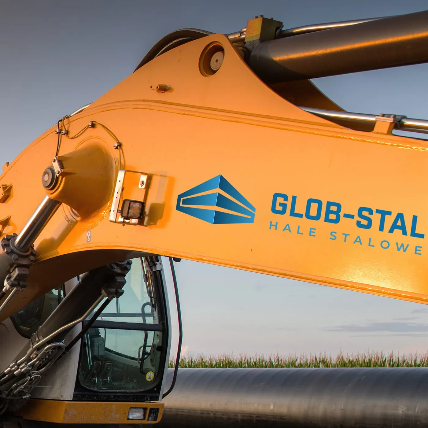 Glob-Stal - pomarańczowe ramię koparki z naklejonym niebieskim logo i logotypem „Glob-Stal - Hale stalowe" na tle nieba.