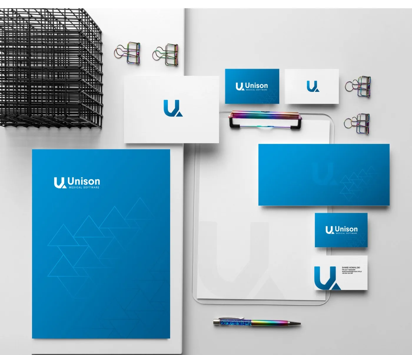 Unison - papeteria firmowa: teczka, papier firmowy, koperta, wizytówki i długopisy w bieli i niebieskim.