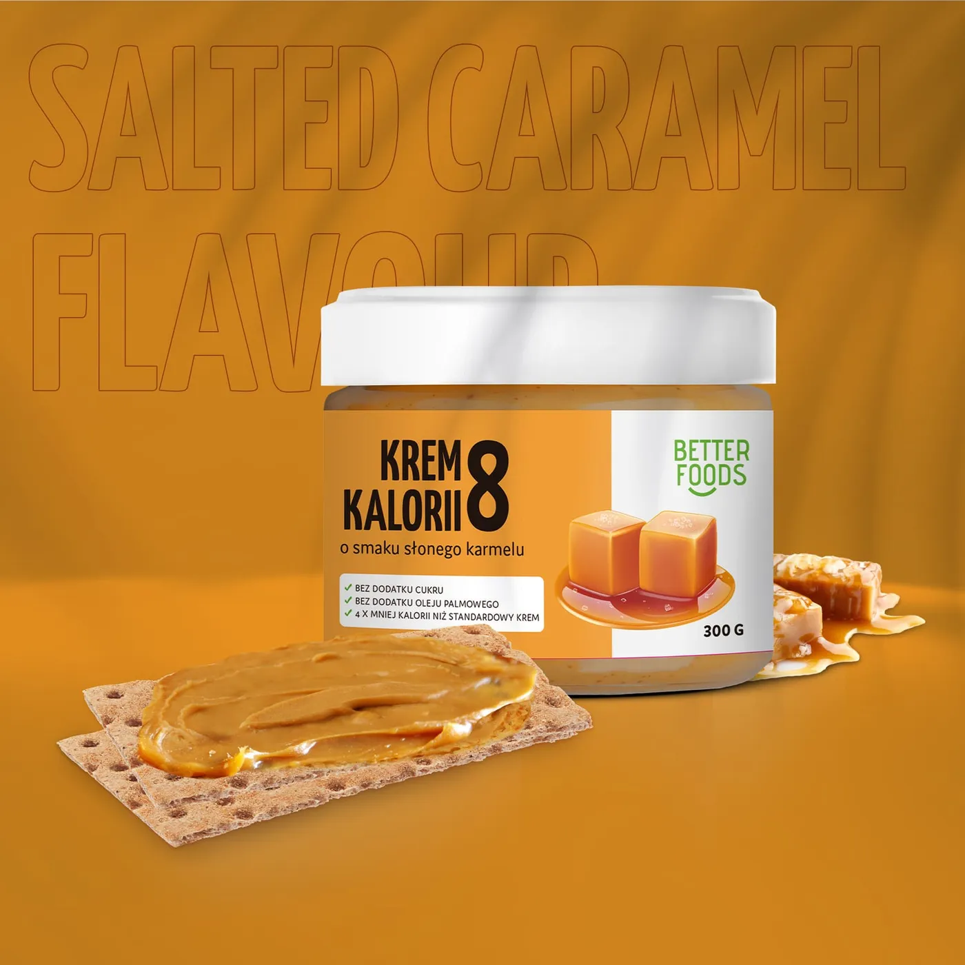 Słoik kremu Better Foods o smaku słonego karmelu, z kostkami karmelu i krakersem posmarowanym kremem, na pomarańczowym tle z napisem „Salted Caramel Flavour".