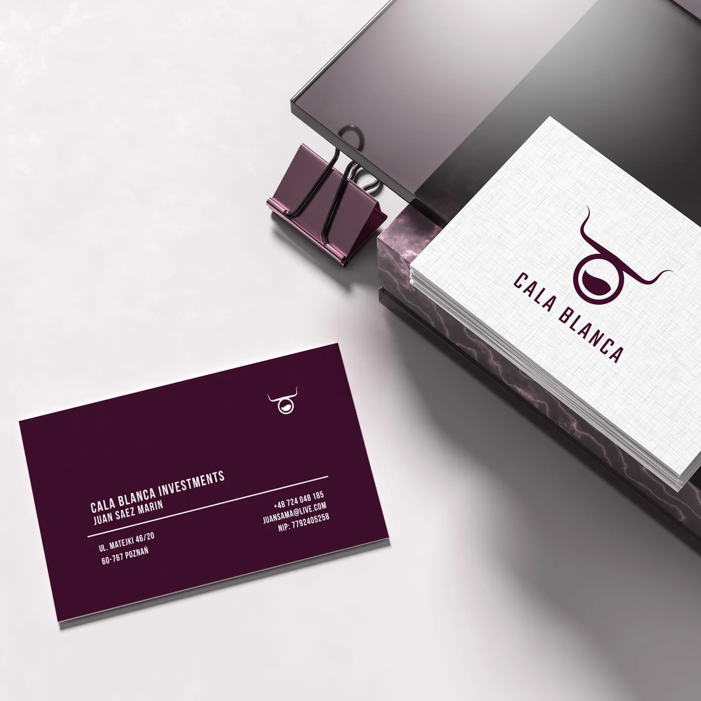 Stos białych wizytówek z logo Cala Blanca na marmurowym podeście obok bordowej wizytówki z danymi kontaktowymi firmy „Cala Blanca Investments".
