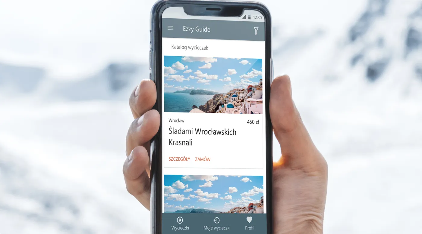 EzzyGuide - dłoń trzymająca telefon na tle ośnieżonych gór, na ekranie katalog wycieczek z kartą oferty „Śladami Wrocławskich Krasnali", ceną i przyciskami „Szczegóły" oraz „Zamów".